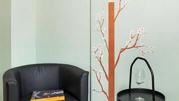 A room with a black leather sofa, a small black table with a wine glass, and a wall mural of a tree with a bird.