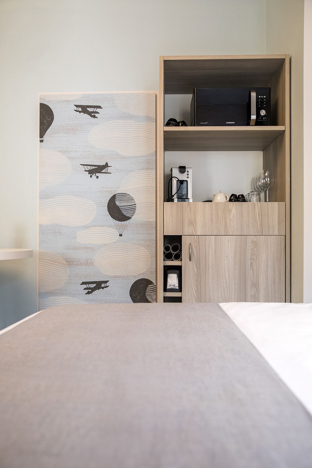 Ein Zimmer mit einem Bett, einem Holzschrank mit Kaffeemaschine und einer Wand mit einem Muster aus schwarz-weißen Flugzeugen.
