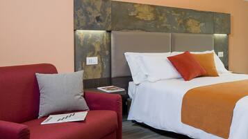 Una camera d'albergo con un divano rosso, un letto con biancheria da letto bianca e arancione, e una parete strutturata sopra il letto.