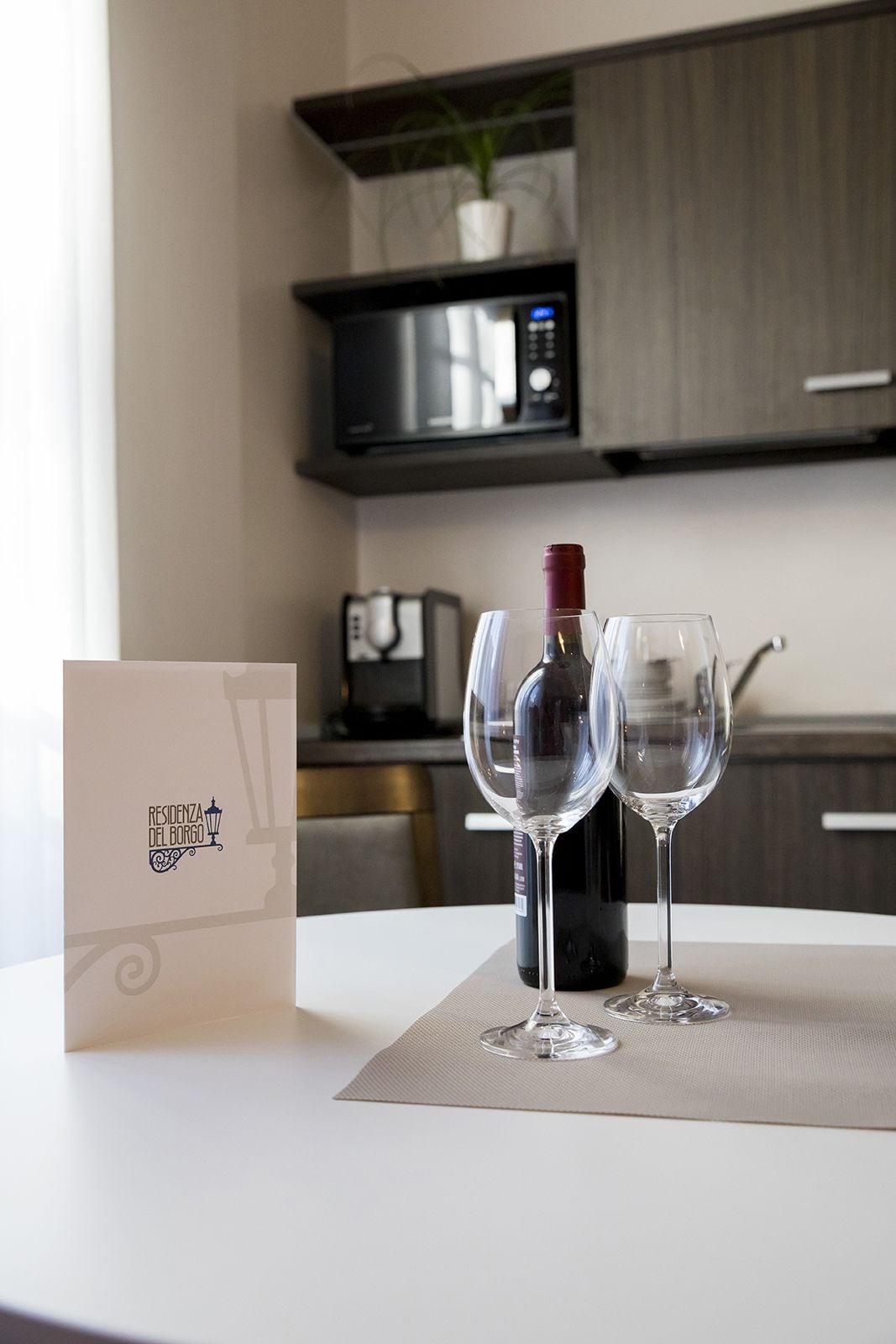 A table with a bottle of wine and two wine glasses, a menu, and a potted plant in the background.
