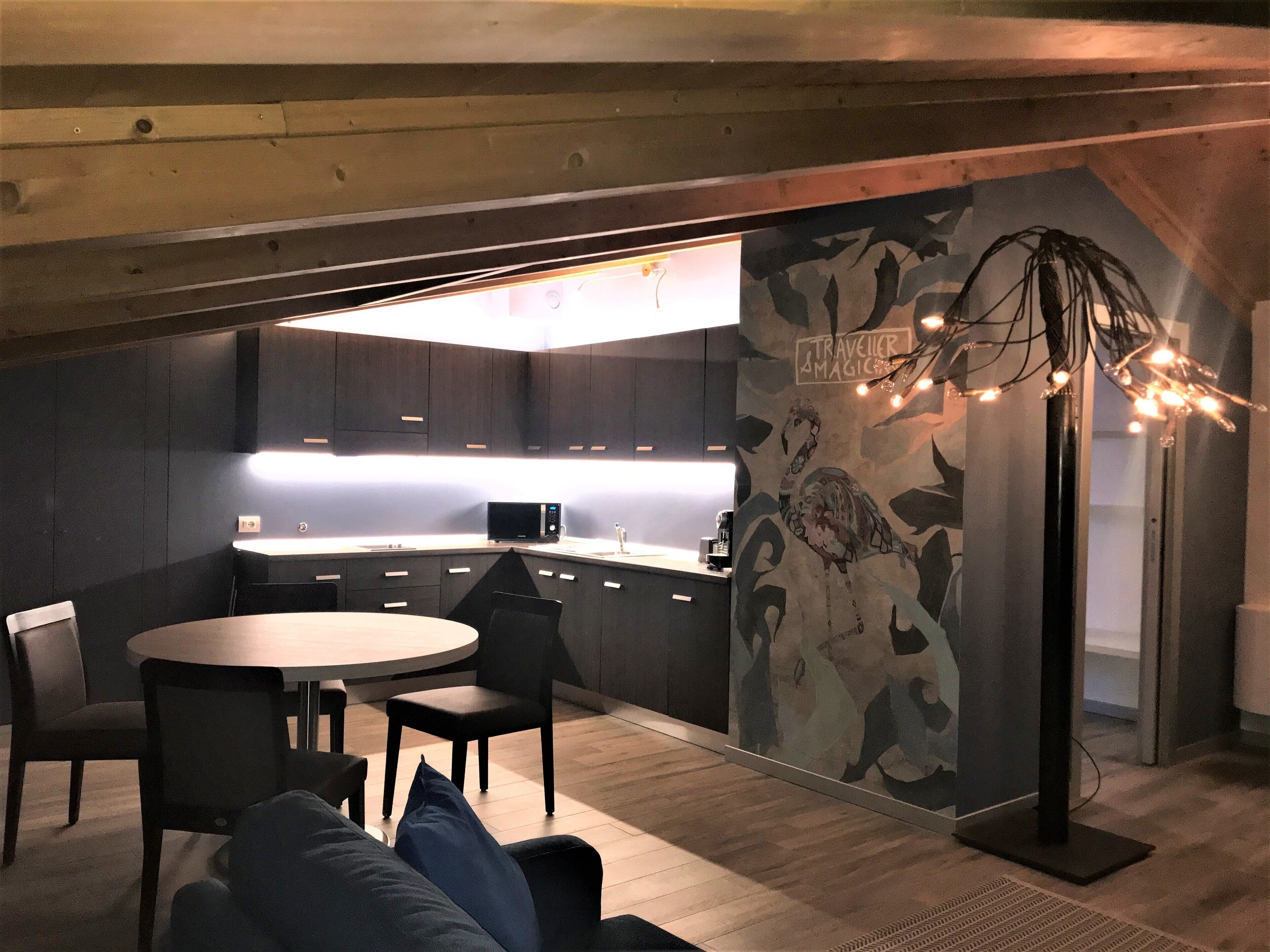 A modern kitchen with dark cabinetry, a round dining table with chairs, and a wall-mounted light fixture.