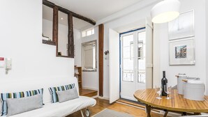 A cozy living room with a white sofa, a wooden dining table with two wine glasses and a bottle, and a white kettle. - LxWay Apartments Graça - Santa Marinha (Lisbon)