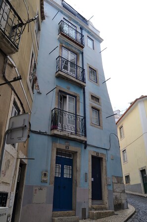 A multi-story building with a blue facade, a central blue door, and balconies with black railings.