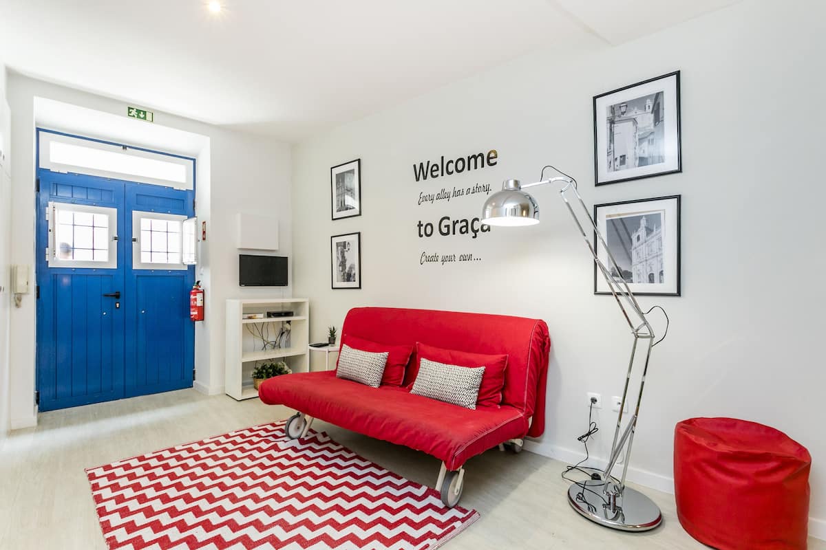 Ein modernes Zimmer mit einem roten Sofa, einem roten Sitzsack, einer Stehlampe und einem Teppich mit Zickzackmuster.