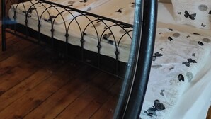 A bedroom with a wooden ceiling, a bed with a metal frame, and a nightstand with a lamp. - Maurushaus (Fuessen)