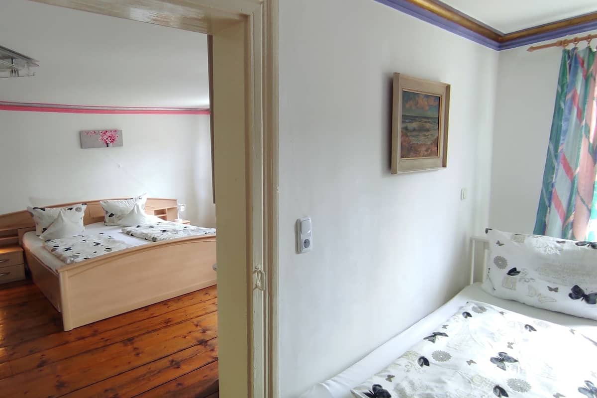 Un dormitorio con suelo de madera, una cama con ropa de cama floral, una mesita de noche con una lámpara y un pequeño escritorio con una silla.