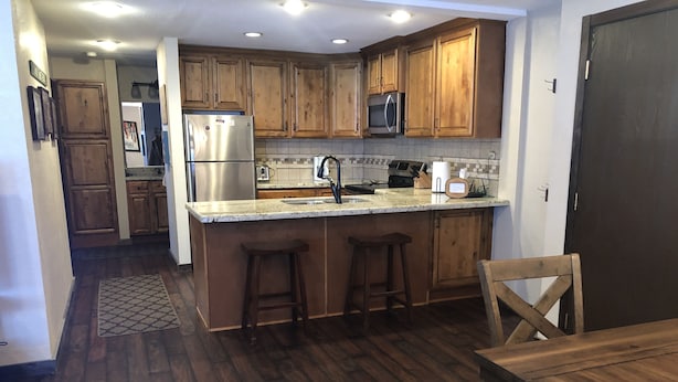 A kitchen with wooden cabinets, a stainless steel refrigerator, a microwave, and a sink. There are two stools and a wooden table with a bench. - Giant Step 3 Condo!  Ski-in/Ski-Out. Completely Remodeled!  WI-FI (Brian Head)