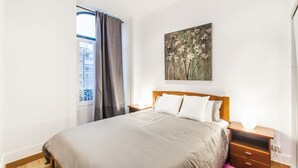 A bedroom with a large bed, a nightstand, a wall-mounted painting, and a window with curtains. - LxWay Apartments Largo de Santa Bárbara (Lisbon)