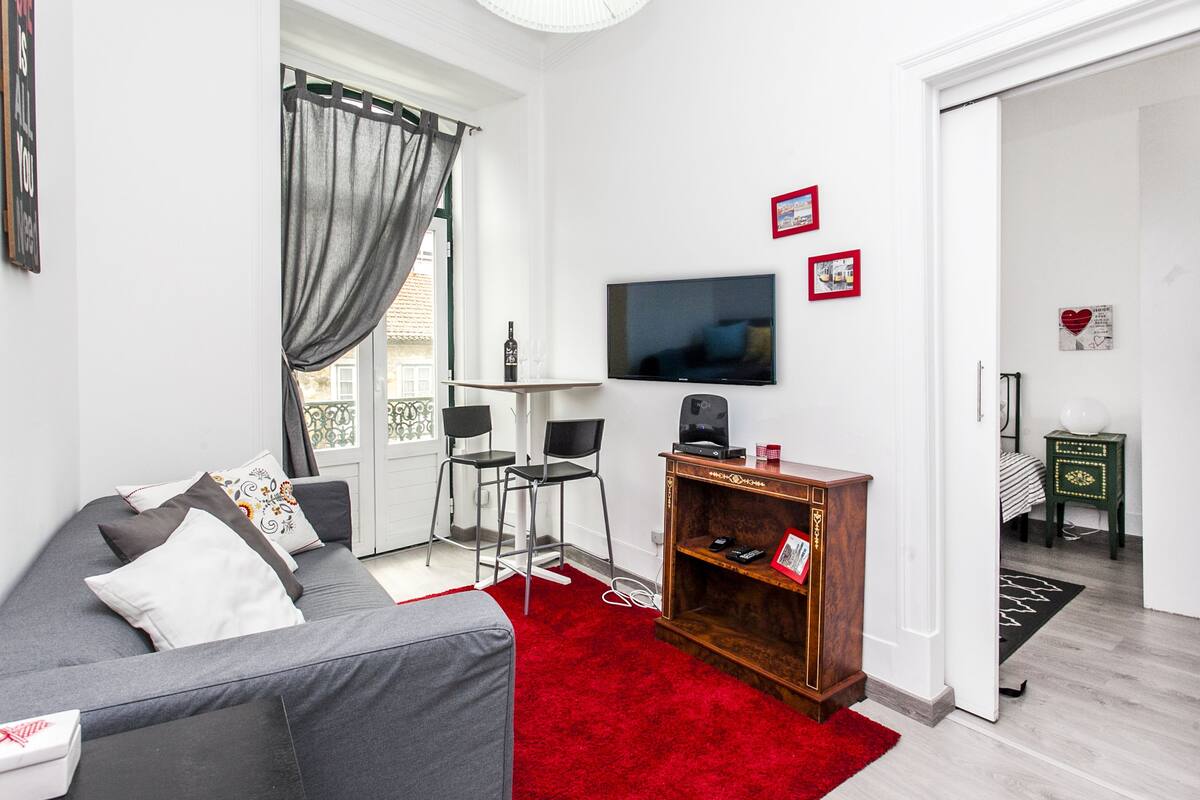 Una sala de estar moderna con un sofá gris, alfombra roja y un televisor de pantalla plana montado en la pared.