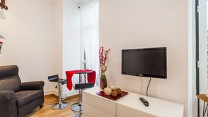 A modern living room with a flat-screen TV, a sofa, a red chair, and a small table with decorative items. - LxWay Apartments Largo de Santa Bárbara (Lisbon)