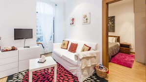 A modern living room with a white sofa, a flat-screen TV, a coffee table, and a red patterned rug. - LxWay Apartments Largo de Santa Bárbara (Lisbon)