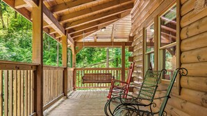 A wooden cabin with a porch, wooden deck, and a bench.