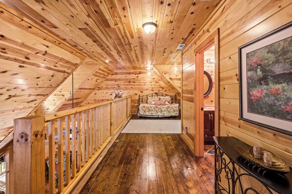 A wooden interior with a wooden staircase, a bed with floral bedding, and a framed picture on the wall. - Hot Tub + Game Room-Free Dollywood Tickets-1 mile to Gatlinburg (Gatlinburg)