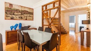 Ein Essbereich mit einem Glastisch und Stühlen, einer Holztreppe und einem Gemälde an der Wand.