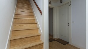 Eine Holztreppe mit Handlauf, eine weiße Tür mit der Aufschrift '1A' darüber und eine Fußmatte auf dem Boden.