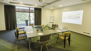 Een vergaderruimte met een grote tafel, stoelen, een projectorscherm waarop 'Castellum Business & City Break Hotel' staat, en een whiteboard.