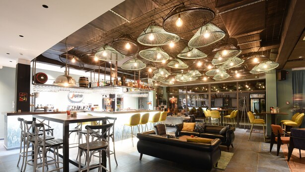A modern bar area with a bar counter, stools, and hanging light fixtures. - Hotel Castellum (Cakovec)