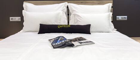 A neatly made bed with white bedding and a single black pillow, a magazine on the bed, and a wooden headboard.