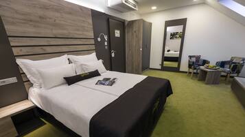 A modern hotel room with a neatly made bed, a small seating area with chairs, and a large mirror reflecting the room.