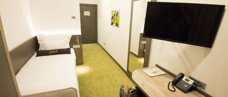 Una habitación de hotel con una cama, un escritorio con teléfono, una televisión y alfombra verde.