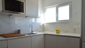 A kitchen with white cabinets, a stainless steel sink, a microwave, and a window providing natural light. - Algarve luxury seaview apartment with pool near beaches  (Porches)