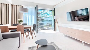 A modern living room with a dining area, a sofa, a TV, and a view of a building through large windows.
