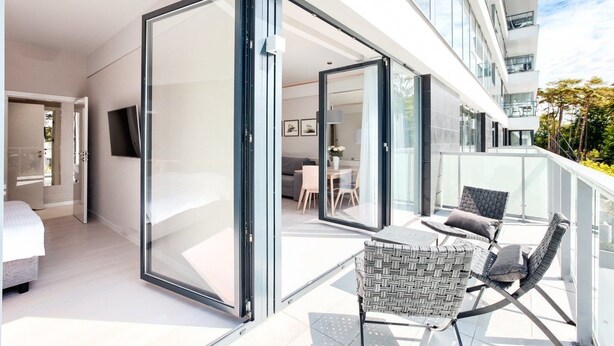 A modern balcony with a glass door leading to a living area, furnished with a table and chairs.