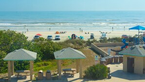 Vista de una playa con mesas de picnic, sombrillas y un parque infantil.