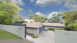 Una propiedad residencial moderna con un césped cuidado, entrada protegida por un portón y cielo despejado.