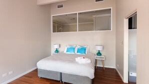 Un dormitorio con una cama grande, dos mesitas de noche con lámparas, un espejo sobre la cama y un armario.