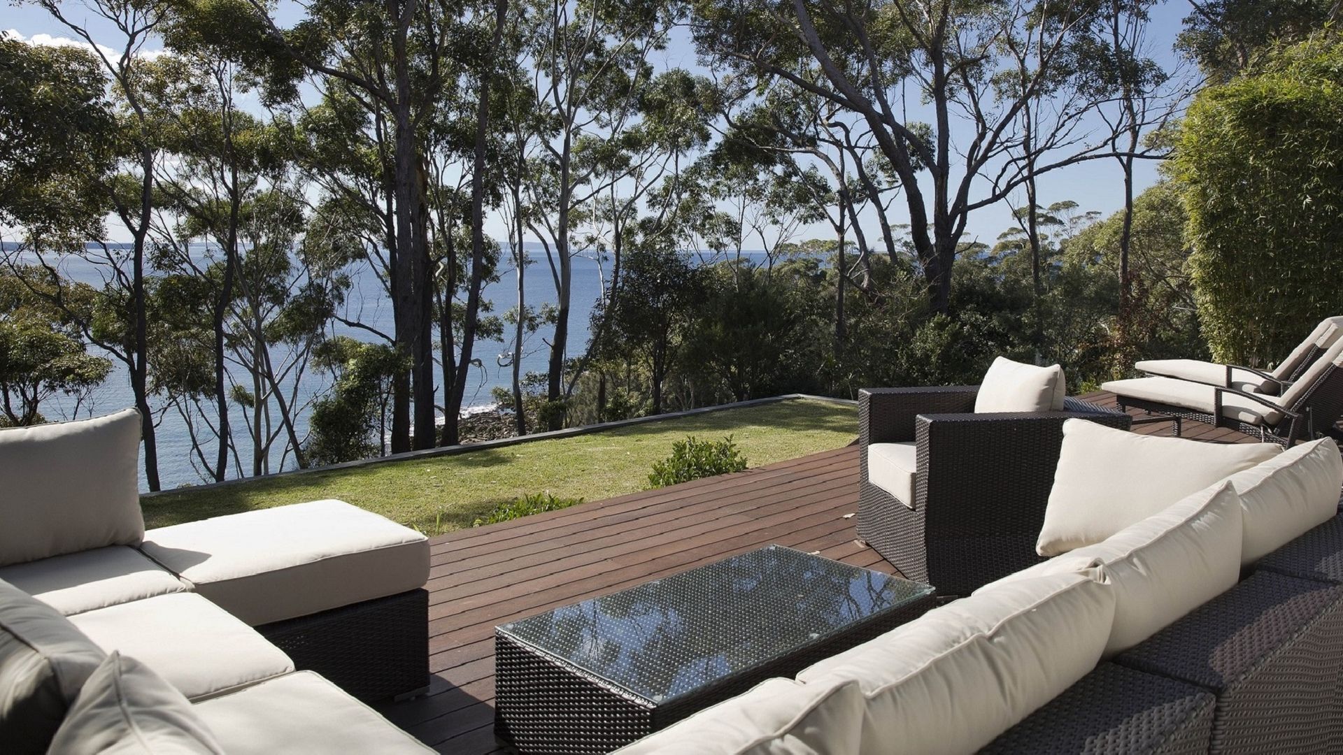 A deck with outdoor furniture, including sofas and a table, overlooking a body of water and trees.