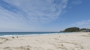 Una playa con cielo despejado, orilla de arena y un edificio al fondo.