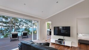 Una sala de estar moderna con un televisor de pantalla plana grande, un sofá de cuero negro y una terraza de madera con dos tumbonas.