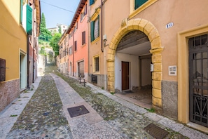 Une ruelle étroite pavée, bordée d’immeubles aux portes cintrées et aux volets fermés.