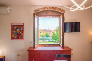 Une pièce avec une fenêtre, un téléviseur fixé au mur et un tableau coloré accroché au mur.