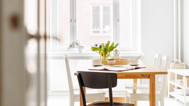 A bright dining area with a wooden table, white chairs, and a black pendant light.