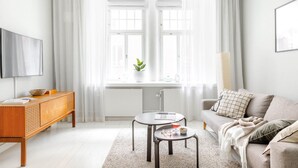 A modern living room with a sofa, a coffee table, a TV, and a window with curtains.