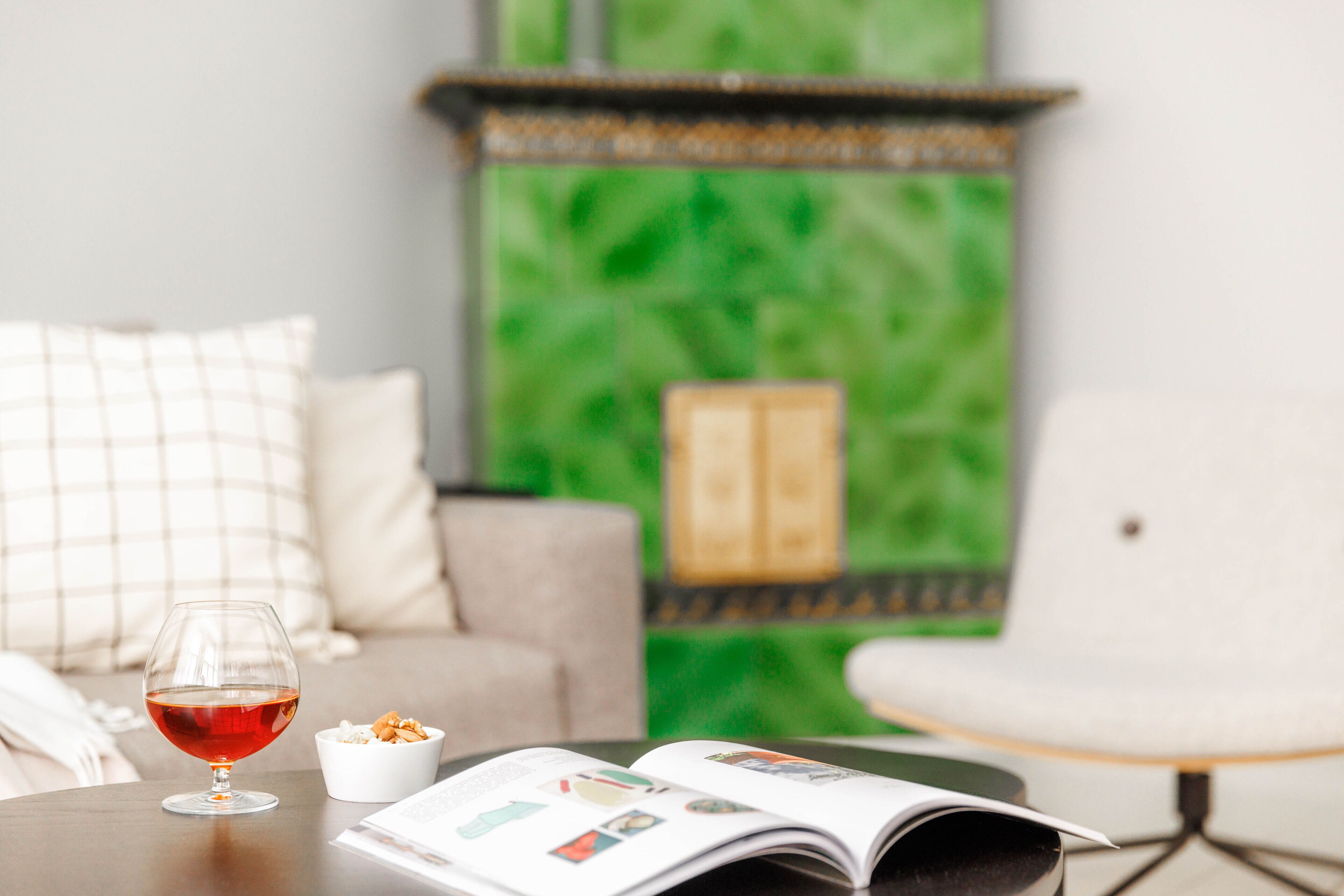 A magazine on a table, a glass of red wine, and a bowl of snacks.