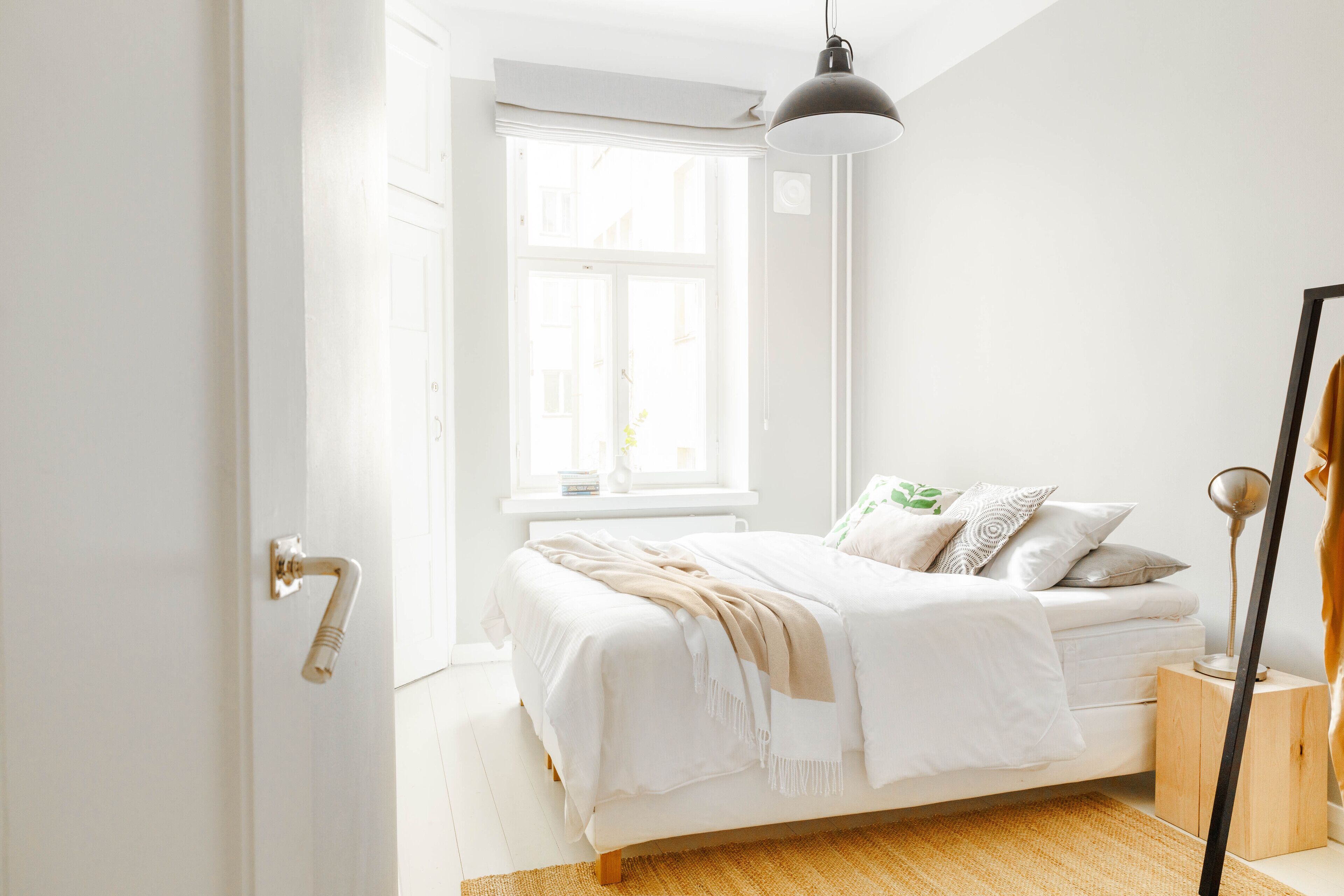 Un dormitorio con cama, ventana, mesita de noche y lámpara.