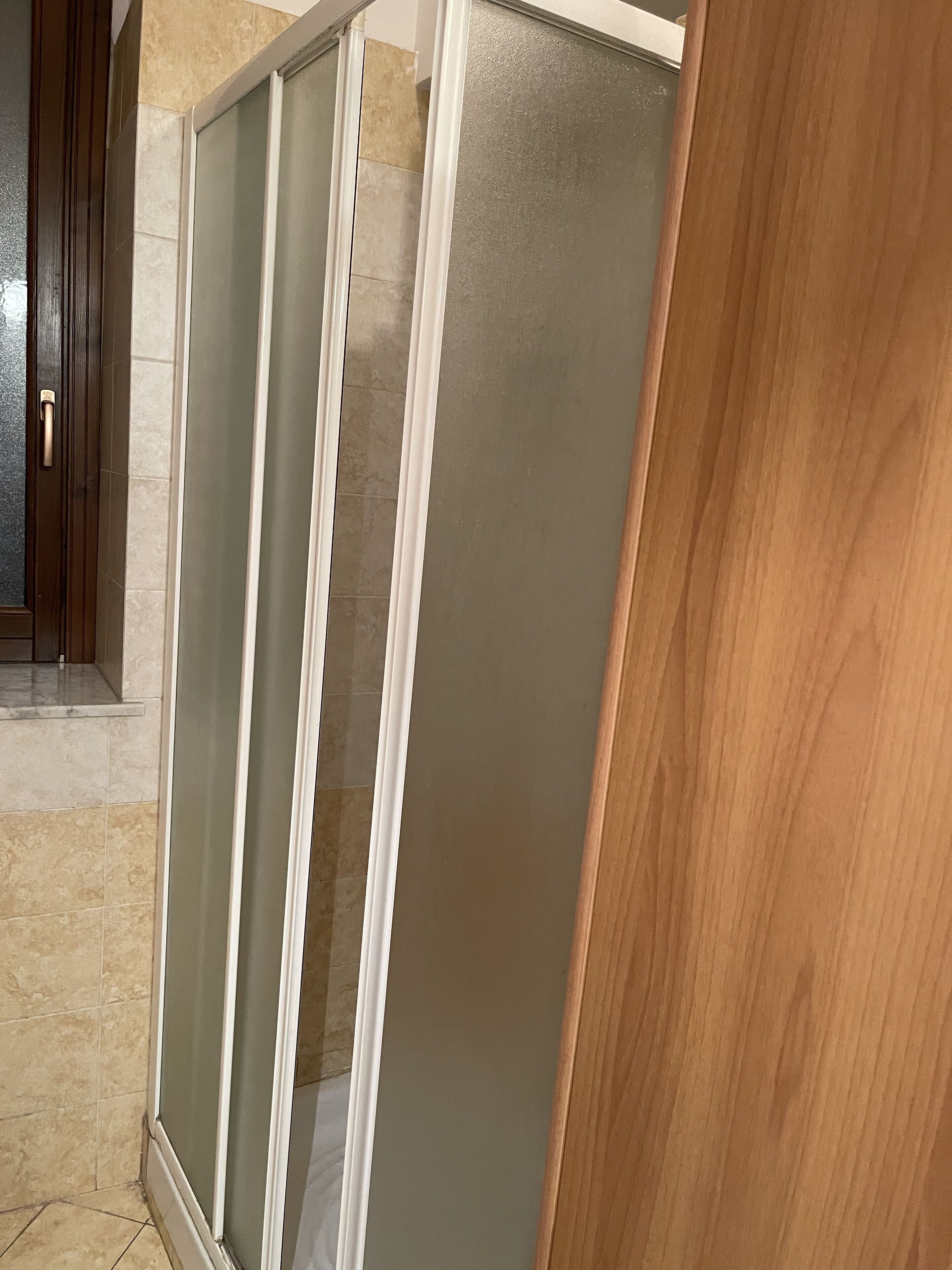 Una esquina de una habitación con una puerta de madera y un separador de vidrio esmerilado.