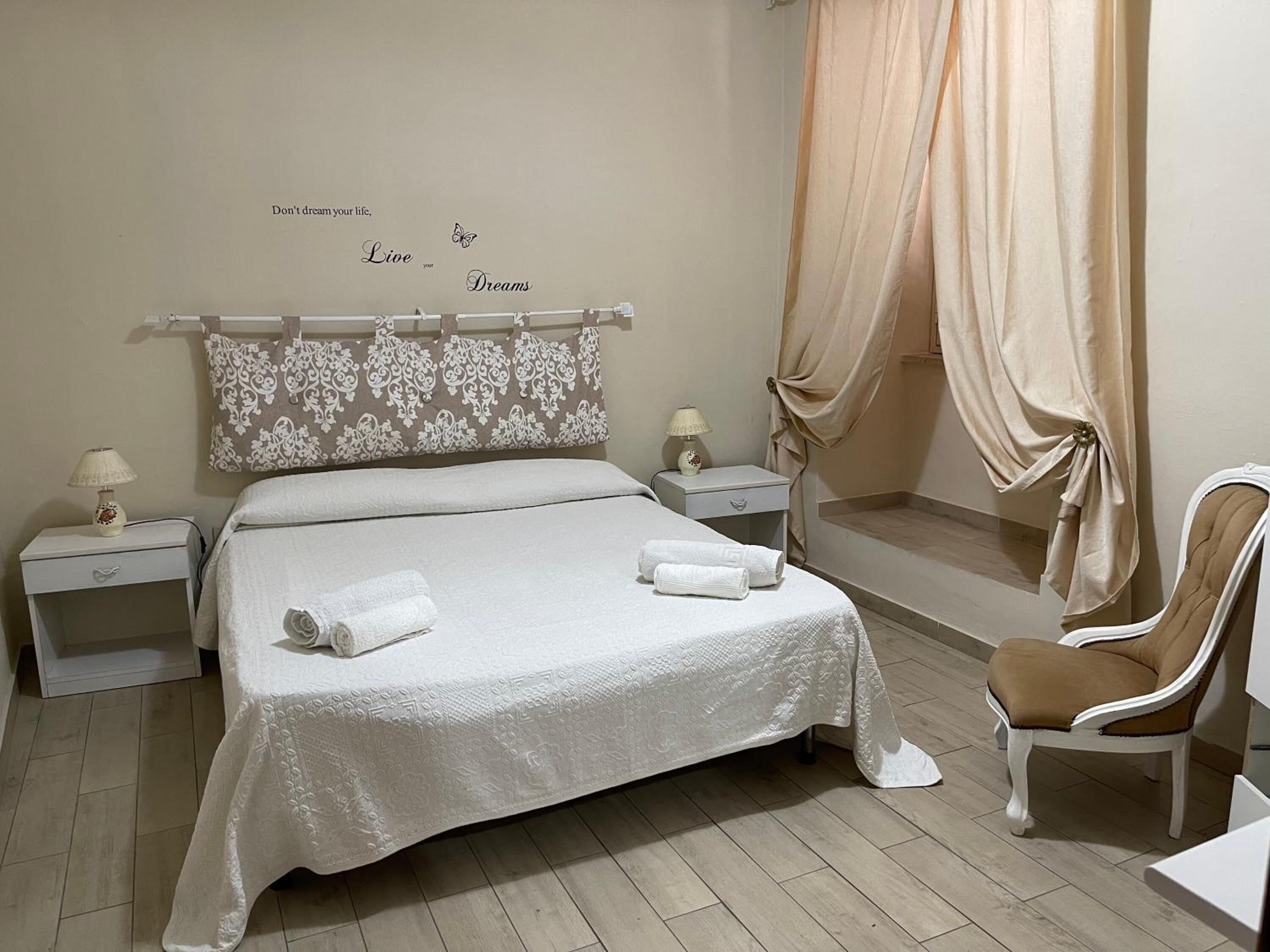 A neatly arranged bedroom with a bed, two bedside tables with lamps, a chair, and a decorative wall with a motivational quote.