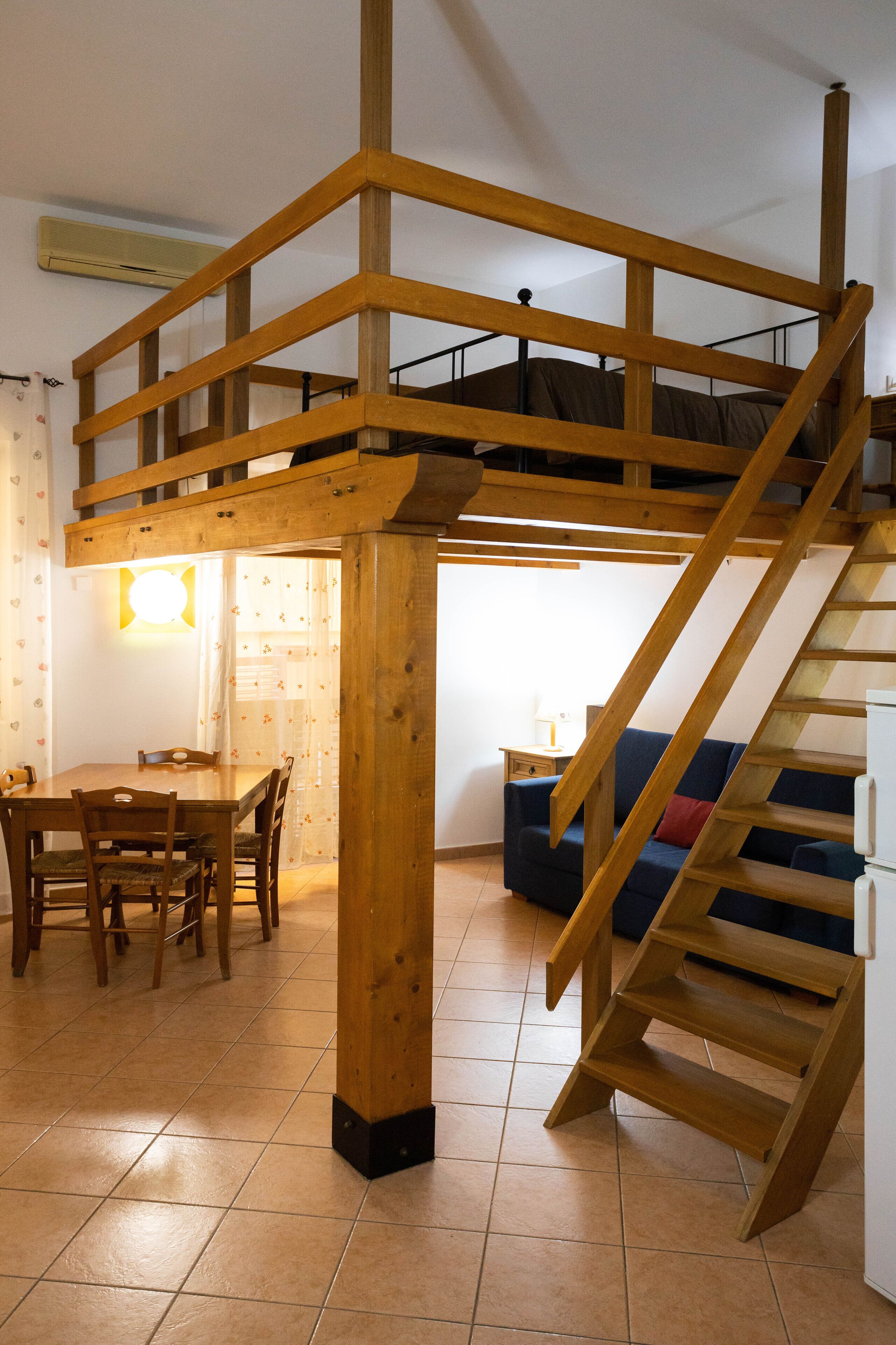 A loft bedroom with a wooden staircase and a dining area with a table and chairs.