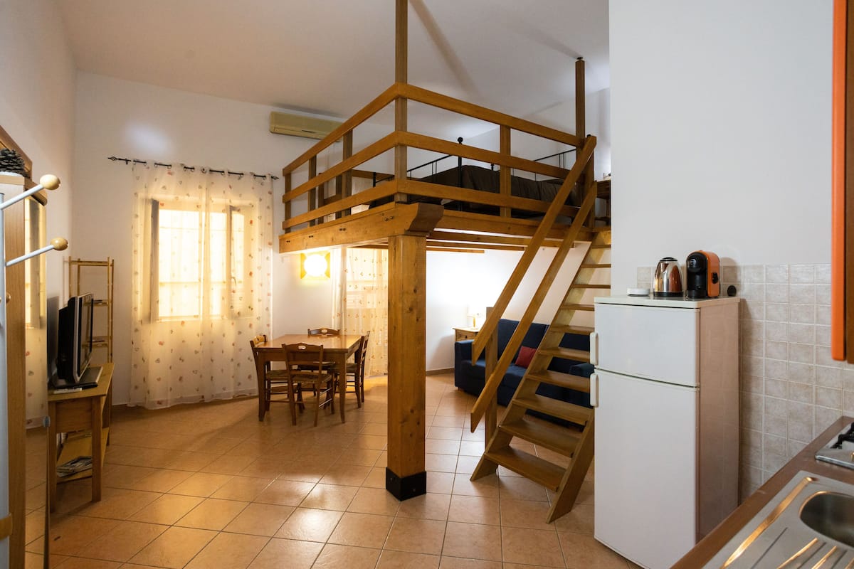 A compact kitchen with a wooden staircase, a dining area, and a small refrigerator.