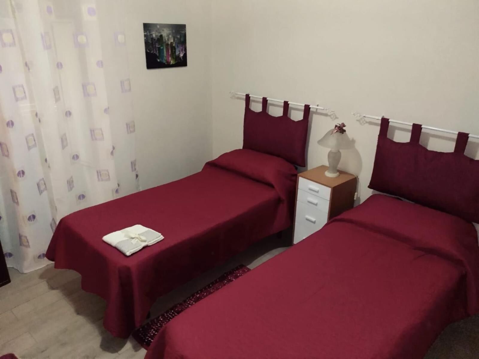 A bedroom with two single beds, a nightstand with a lamp, and a small table with a vase.