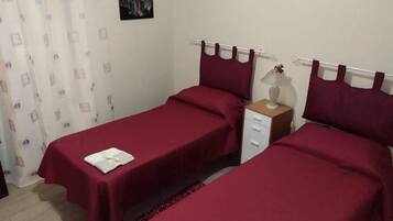 A bedroom with two single beds, a nightstand with a lamp, and a small table with a vase.