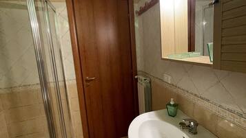 Une salle de bain avec une douche à parois de verre, une porte en bois, un lavabo blanc et un miroir au-dessus.