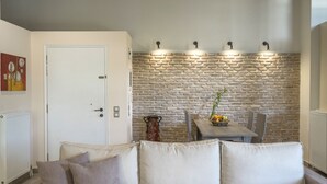 Een woonkamer met een stenen muur, een witte deur, een eettafel met stoelen en een bank met kussens.