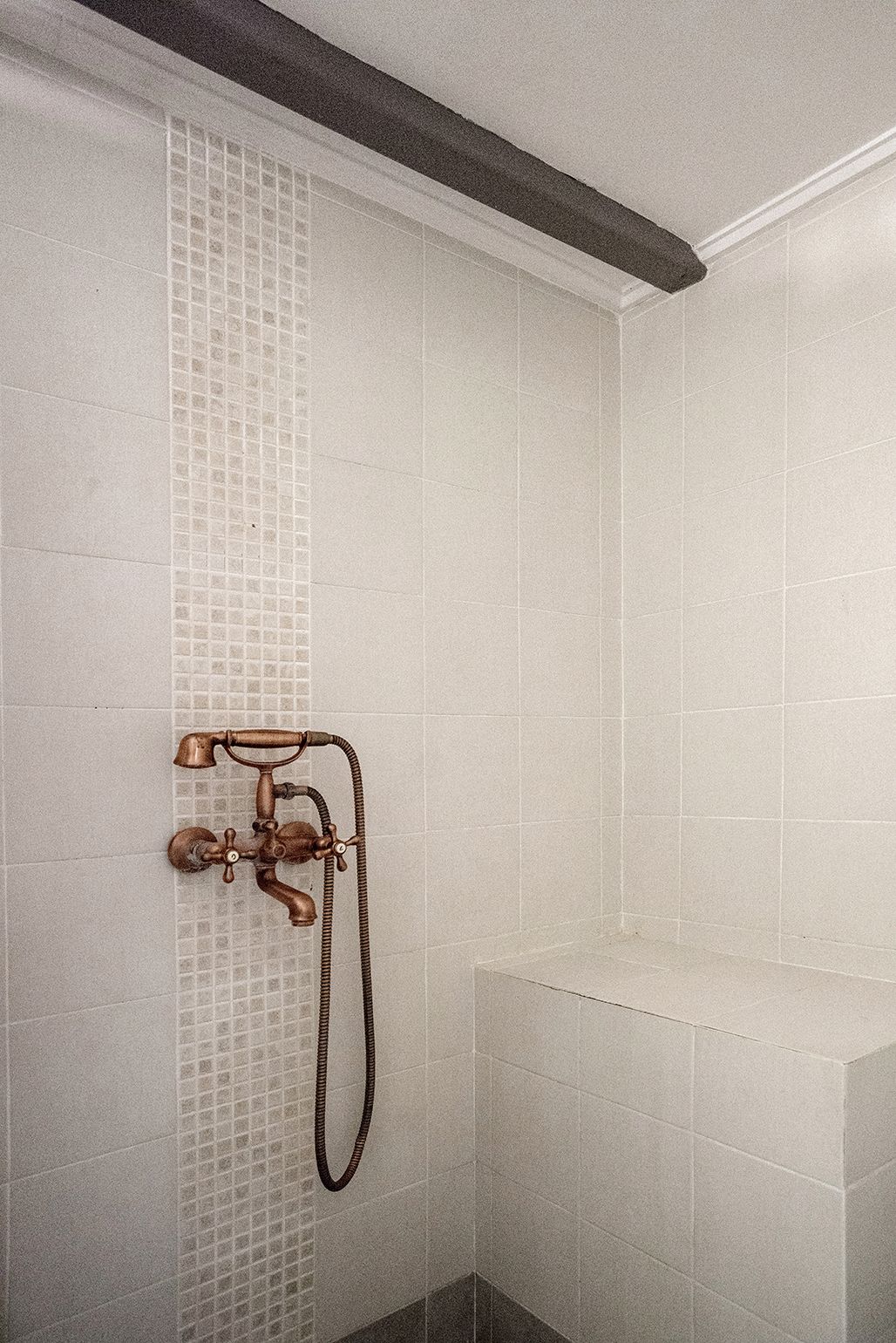 A shower with a vintage faucet and a tiled wall.