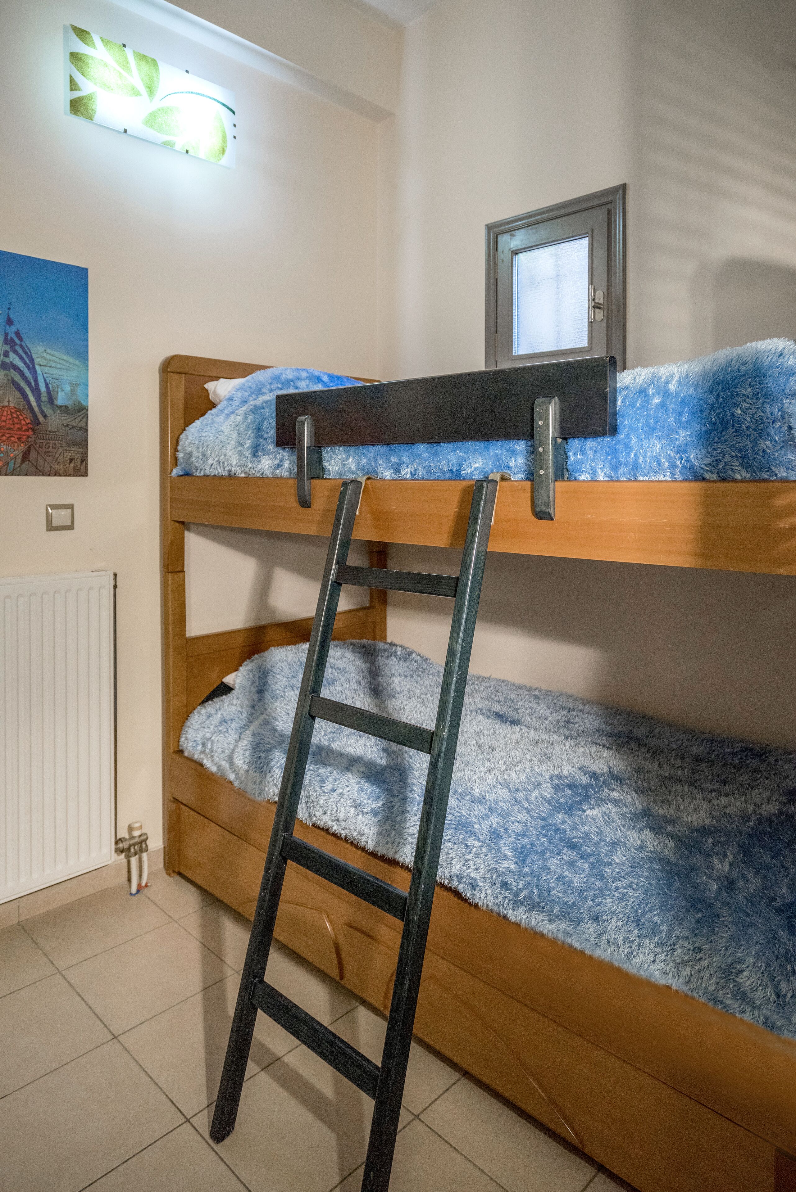 A bunk bed with a ladder, a small window, and a radiator.