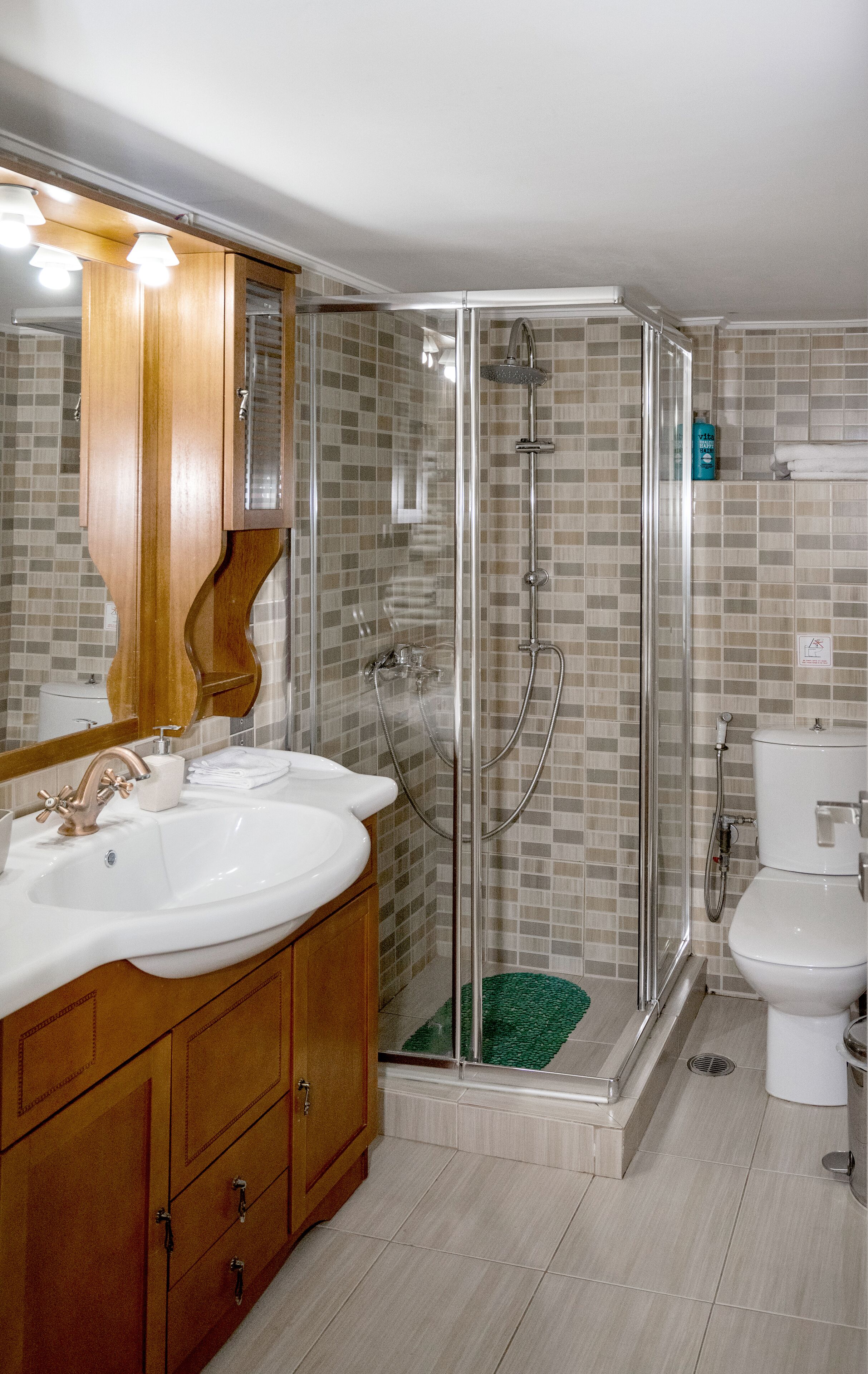 Un baño con tocador de madera, dos lavamanos, ducha con cerramiento de vidrio y un inodoro.